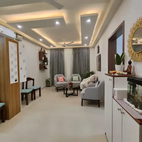 Living room with a multi-tier cove-lit false ceiling, grey armchairs around a black coffee table, and a gold sunburst mirror above a styled console.