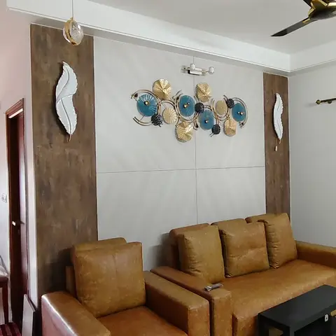 Living room with a mustard-tan leather sofa set facing a textured wood-and-white accent wall featuring a gold-and-blue metal flower wall sculpture