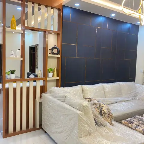 Living room with a navy-and-gold panelled feature wall, a warm-wood slatted display partition, and a new sofa still wrapped in plastic