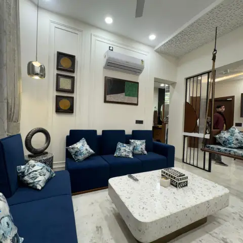 Living room with a navy-blue sofa set, moulded picture-frame wall panelling and a curated gallery wall, opening to a swing nook through a metal jaali screen.