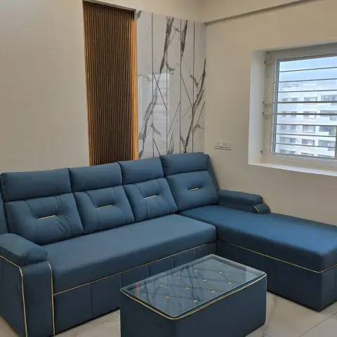 Living room with a navy-blue gold-piped L-shaped sofa, a glass-top storage ottoman coffee table