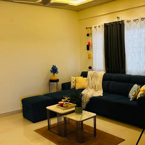 Living room with a navy L-shaped sofa dressed in mustard cushions and a throw, facing nesting marble-top coffee tables on a brown rug