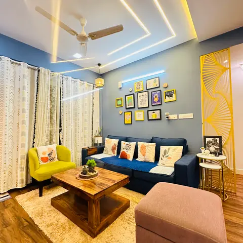 Living room with a navy sofa, mustard accent chair and a curated gallery wall of colorful framed art beneath cove-lit ceiling channels