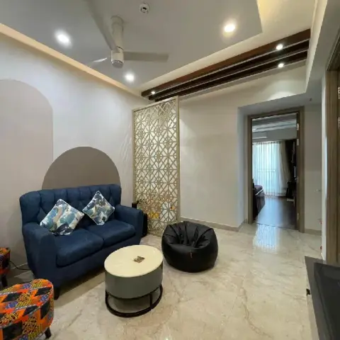 Living room with a navy tufted loveseat, colourful patterned ottomans, a black bean bag, and a gold-toned decorative jaali partition beside a painted wall arch