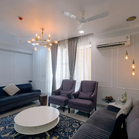 Living room with a navy velvet nailhead sofa and aubergine wingback chairs around an oval coffee table on a floral blue rug, a brass sputnik chandelier