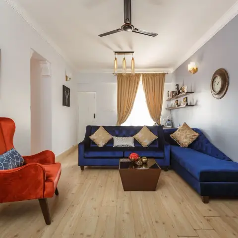 Living room with a navy velvet L-shaped tufted sofa, a rust-orange wingback armchair, a three-bulb Edison pendant cluster overhead