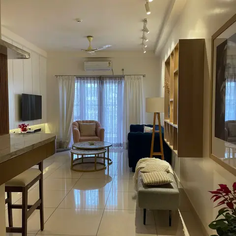Living room with a navy velvet sofa, a blush pink accent armchair, nested marble-top coffee tables, and an open wood shelving unit beside sheer curtains.