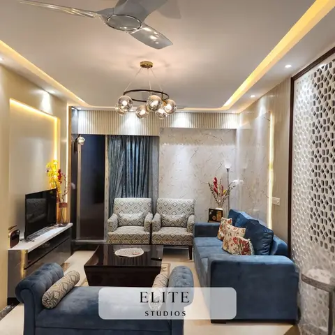 Living room with a perforated white jaali feature wall, marble-clad accent wall, cove-lit ceiling and a blue velvet sofa set around a black coffee table.