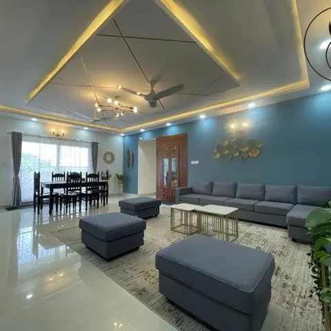 Living room with a pyramid pop false ceiling with gold cove lighting, a teal accent wall styled with a metal disc art arrangement
