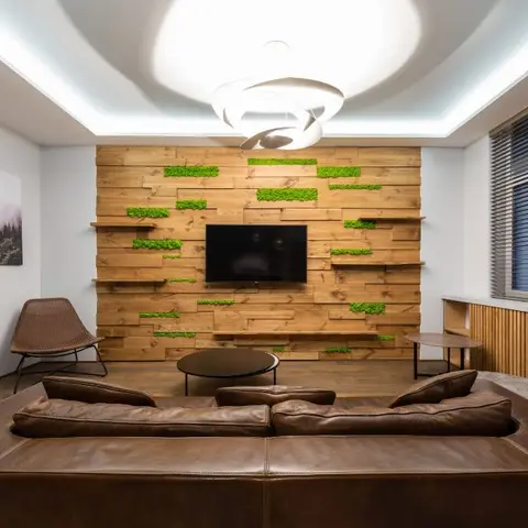 Living room with a reclaimed-wood plank feature wall accented by patches of preserved green moss behind the TV, a sculptural ribbon pendant light