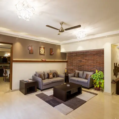 Living room with a red brick feature wall behind a grey sofa set, a Ganesh relief flanked by photo frames on a mocha accent wall