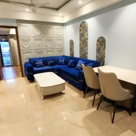 Living room with a royal blue velvet L-sofa against a grid of medallion wall panels, three arched niches papered in banana-leaf print alongside