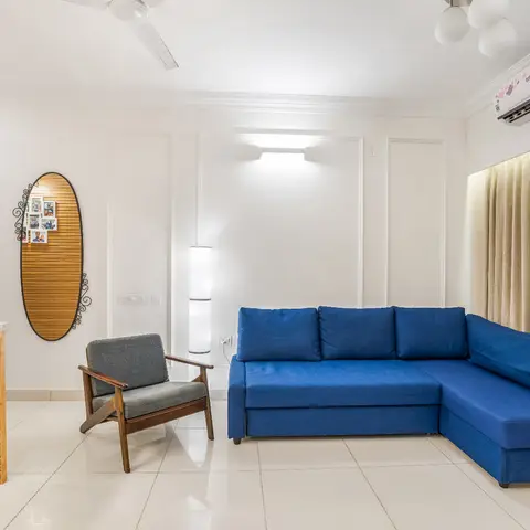 Living room with a royal blue L-shaped sofa, a mid-century wood-frame armchair and an oval mirror with a family photo collage.