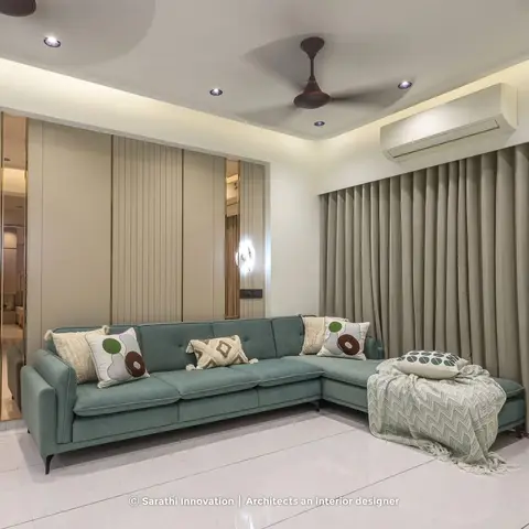 Living room with a sage-teal fabric sectional sofa and patterned throw pillows, set against a fluted wall panel with brass inlay strips and a mirror insert