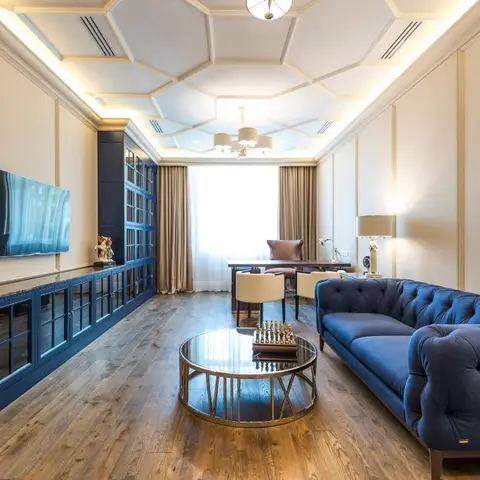Living room with a sculpted hexagonal cove-lit ceiling, navy tufted chesterfield sofa and a long navy glass-front media wall with wall-mounted TV.