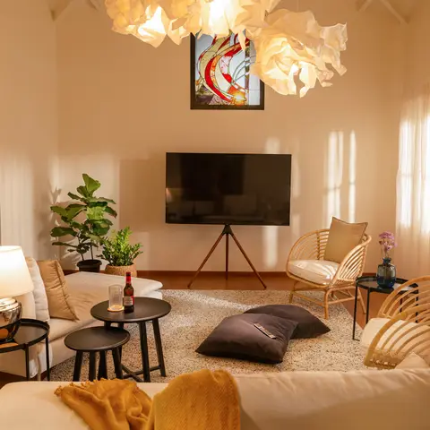 Living room with a sculptural crumpled-paper cloud pendant light over a stained-glass art panel and floating TV, rattan chairs and terrazzo-look rug