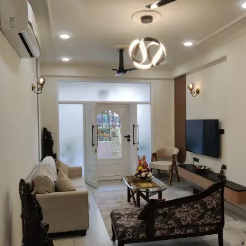 Living room with a sculptural ring pendant light, wall-mounted TV over a floating wood console, and a carved dark-wood bench facing a cream sofa