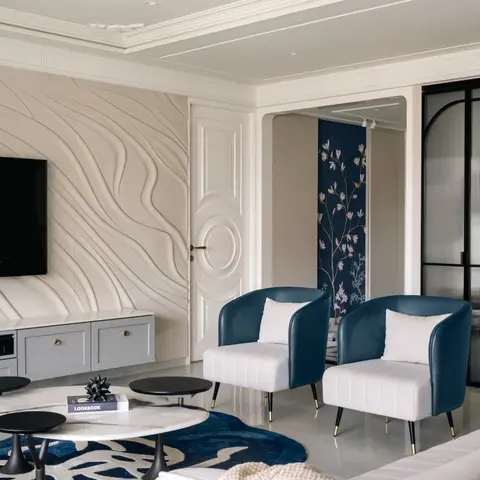 Living room with a sculptural sand-dune wave-textured wall panel behind the TV, navy velvet accent chairs on white bases and a bold navy abstract rug