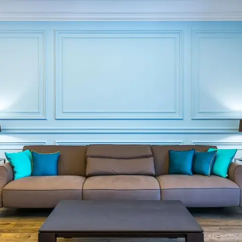 Living room with a sky-blue raised-panel wainscoted wall, a taupe sofa styled with turquoise and teal cushions, and a dark wood coffee table on wood flooring.