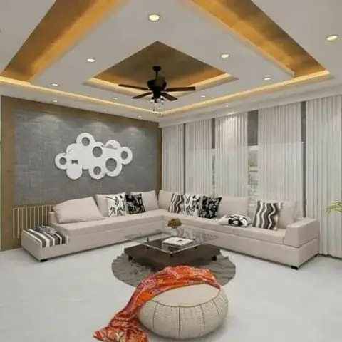 Living room with a stepped gold-cove POP ceiling, a grey textured accent wall with a circular mirror art piece, and a beige L-shaped sectional.