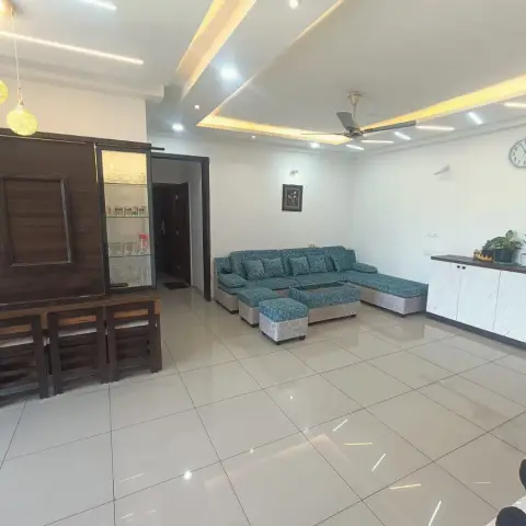 Living room with a stepped POP false ceiling and cove lighting, a teal L-shaped sofa with ottoman, and a dark wood crockery display unit.