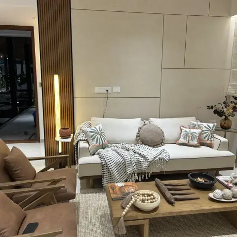 Living room with a stone-panel accent wall, a cream sofa styled with palm-print cushions, leather wood-frame armchairs