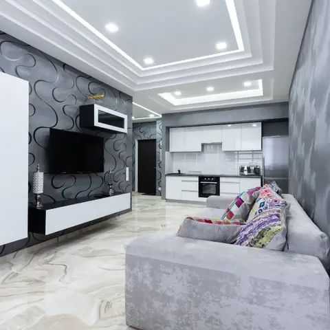 Living room with a swirl-pattern grey wallpaper wall behind a floating black-and-white TV console, kitchen visible beyond.