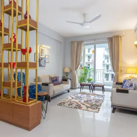 Living room with a tall brass-framed wood shelving console dividing the entry, cream sofas around a printed rug