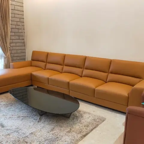Living room with a tan leather L-shaped sofa around an oval black glass coffee table on a cream shag rug