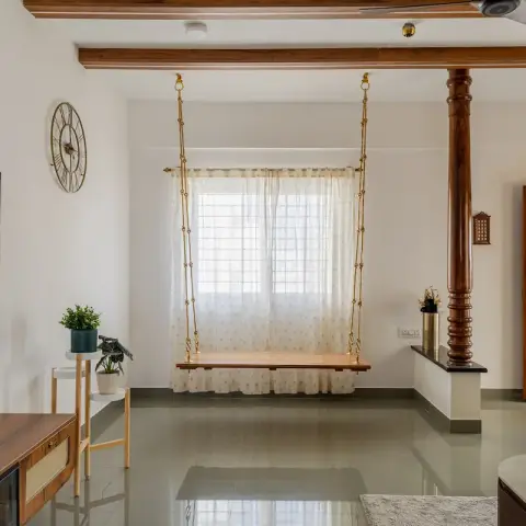 Living room with a teak jhoola hung on brass chains in front of a sheer-curtained window, exposed timber ceiling beams