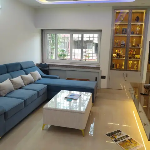 Living room with a teal L-shaped sofa facing a fluted white coffee table on brass legs