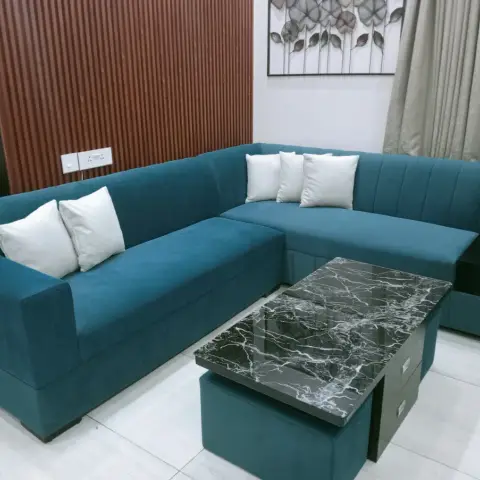 Living room with a teal L-shaped sofa against terracotta fluted panelling, black metal leaf wall art and a black marble-look coffee table with teal ottomans