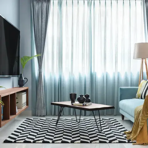 Living room with a teal tufted sofa, a black-and-white chevron rug, a hairpin-leg wood coffee table, and ombre sheer curtains.