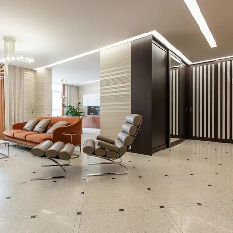 Living room with a terrazzo floor, dark wood slat partition wall, a burnt-orange velvet sofa, and chrome-framed lounge chairs facing a glass coffee table.