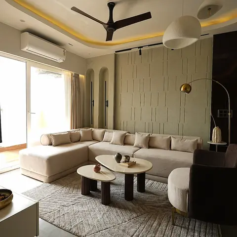 Living room with a textured fluted stone-clad accent wall, cove-lit ceiling, a cream L-shaped sectional sofa around two round nesting coffee tables