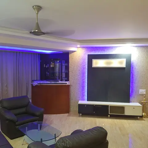Living room with a textured stone TV feature wall lit by blue cove and accent LEDs, black leather sofas, a glass coffee table