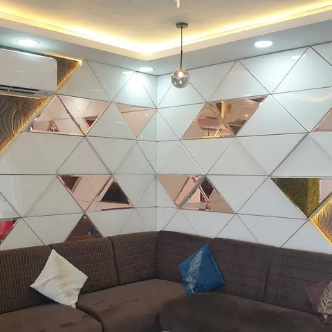 Living room with a triangular white-and-mirror tile feature wall bordered by backlit patterned wallpaper, above a brown channel-tufted sectional sofa.