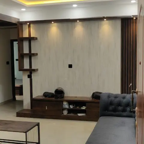 Living room with a tufted grey sofa, a dark wood TV console against a light stone-textured feature wall lit by spotlights