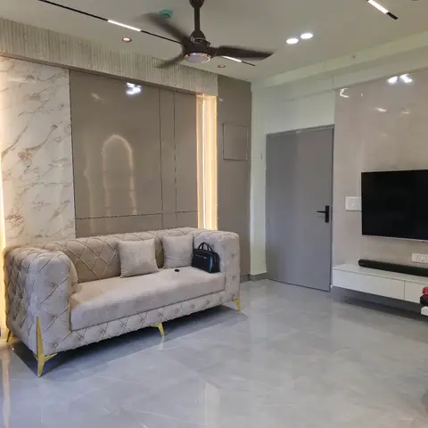 Living room with a tufted grey chesterfield sofa on gold legs, a book-matched marble accent wall, a glossy taupe panel niche