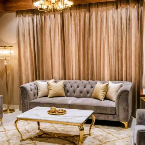 Living room with a tufted grey chesterfield sofa set on gold-legged frames, a marble-and-gold coffee table, a crystal chandelier