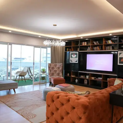 Living room with a tufted rust velvet sofa and patterned wingback chairs facing a full-height black gloss bookshelf-TV wall, under a crystal cluster pendant.