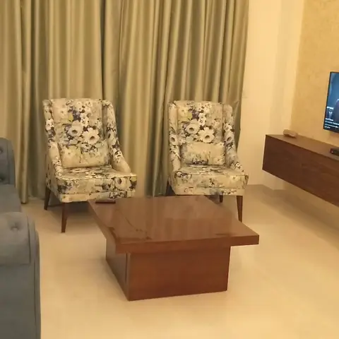 Living room with a tufted teal chesterfield sofa and floral wingback chairs around a wood coffee table