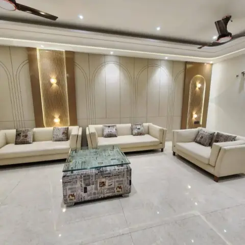 Living room with a U-shaped cream sofa arrangement facing an arched, gold-fluted panelled wall under a cove-lit ceiling, on a polished marble floor.