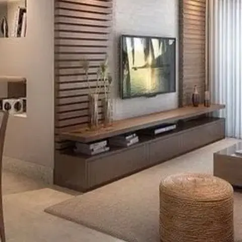 Living room with a vertical fluted-wood accent wall, a floating dark-wood TV console under cove lighting, and a woven jute pouf ottoman on a beige area rug.