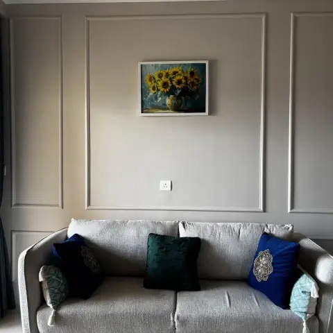 Living room with a wainscot-style panel moulding wall, a framed sunflower still-life painting, and a grey sofa styled with navy
