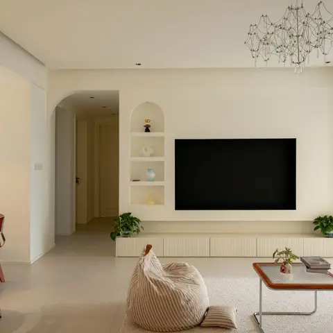 Living room with a wall-mounted TV over a fluted low console, an arched recessed shelf displaying curated ceramics, a wireframe pendant chandelier