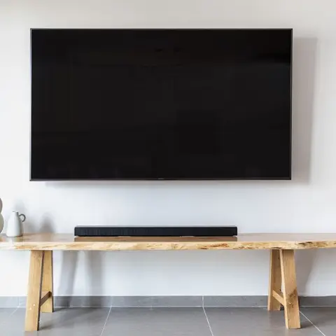 Living room with a wall-mounted TV and soundbar above a live-edge wood bench console styled with two ceramic jugs.