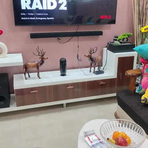 Living room with a walnut-and-white TV console styled with deer figurines and a mounted TV, in front of a charcoal sofa piled with colorful printed cushions.