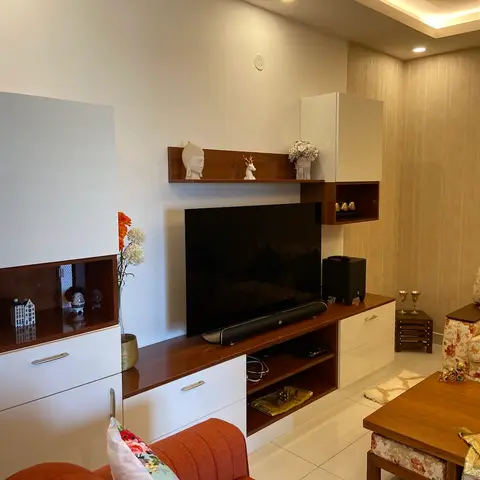 Living room with a white-and-walnut TV wall unit topped with curated curio figurines, a glass-front display cabinet