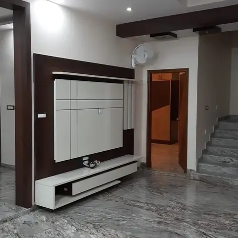 Living room with a white gloss TV unit set into a dark wood-framed wall panel, open to a staircase and hallway across grey-veined marble flooring.